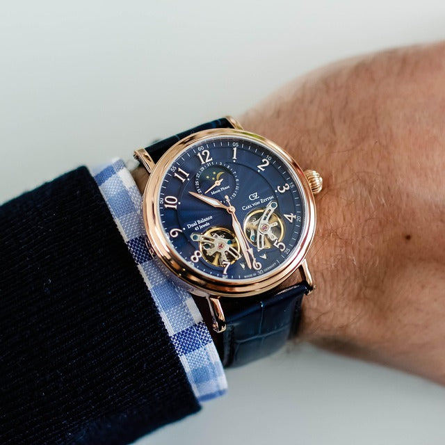 A person in a dark suit adjusts their jacket, wearing a gold wristwatch and a simple gold ring on their left hand.