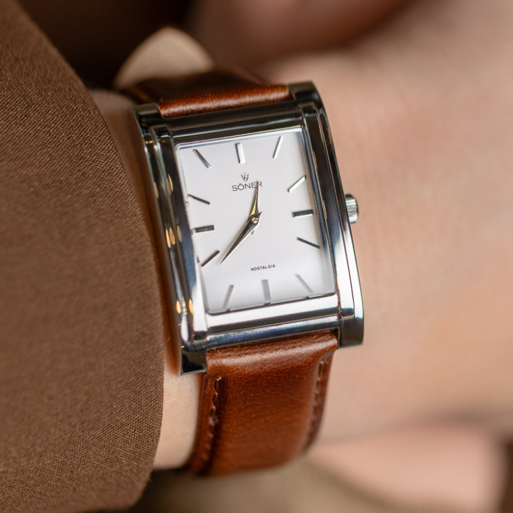 A rectangular watch with a white dial, silver casing, and brown leather strap elegantly displays the time as 10:09 on the wrist. The brand name SONER graces the dial, adding a touch of sophistication.