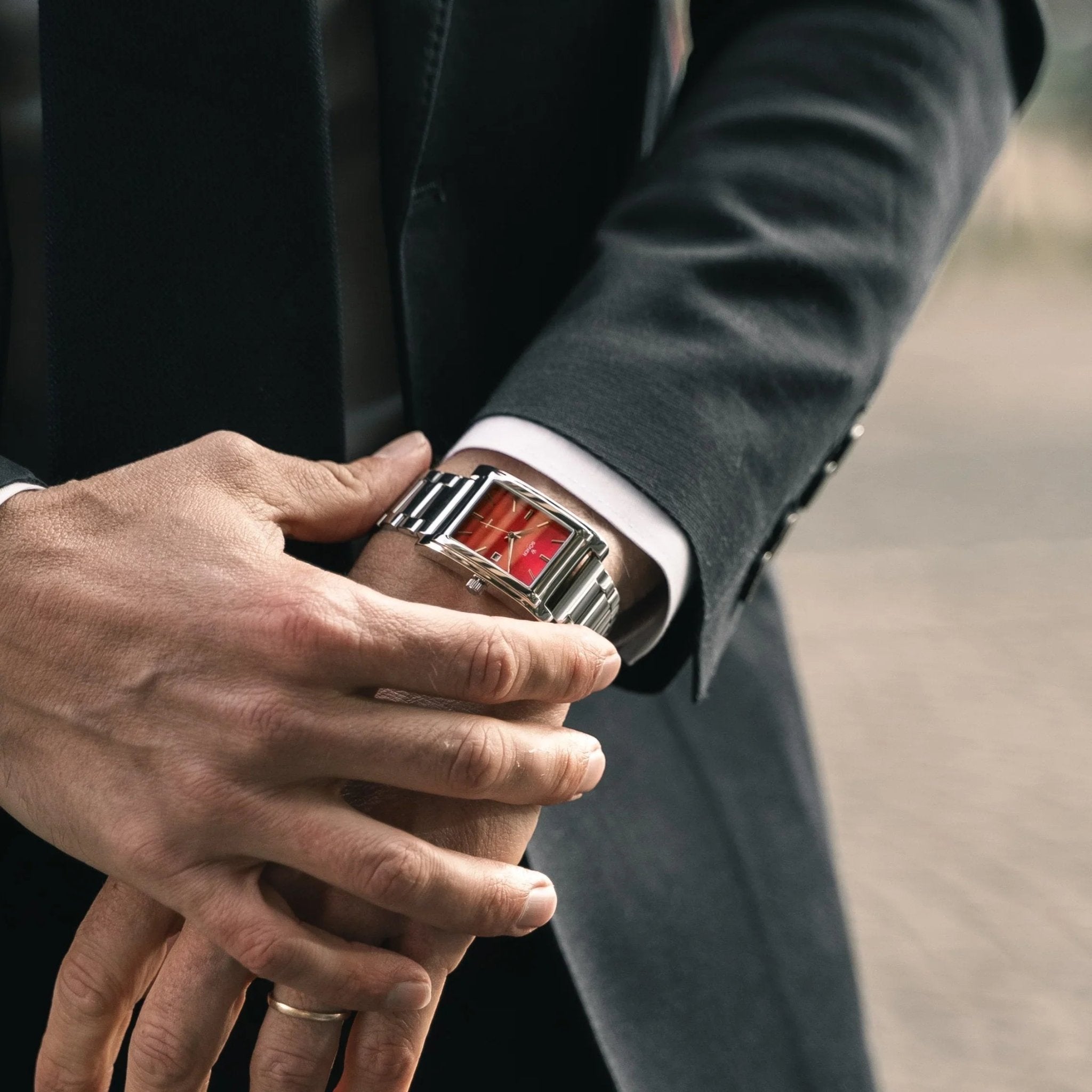A man in a suit wearing the Amorous Rio Automatic rectangular watch with a polished steel bracelet and a vibrant ruby-red dial.