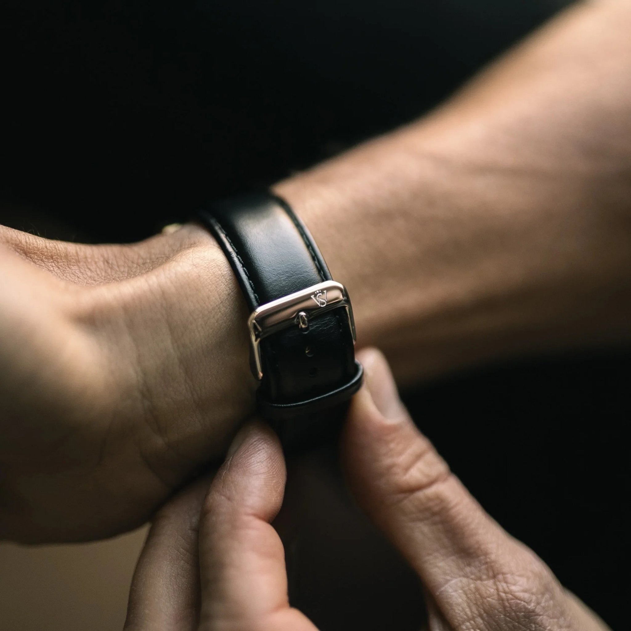 Close-up of the Amorous Rio Automatic's genuine black leather strap with polished buckle being fastened on the wrist.