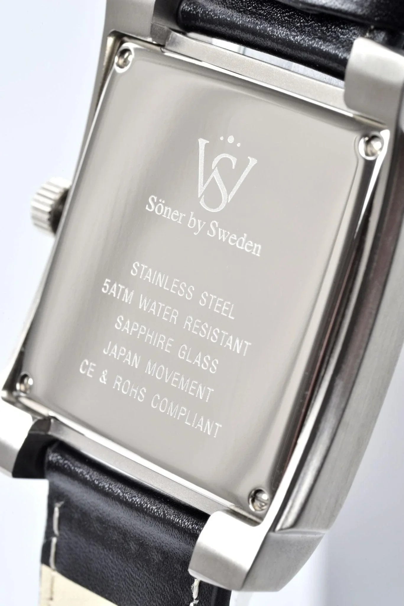 Close-up of the Legacy Prisma watch case back showing engraved details including stainless steel construction, 5 ATM water resistance, sapphire glass, Japanese movement, and a black leather strap.