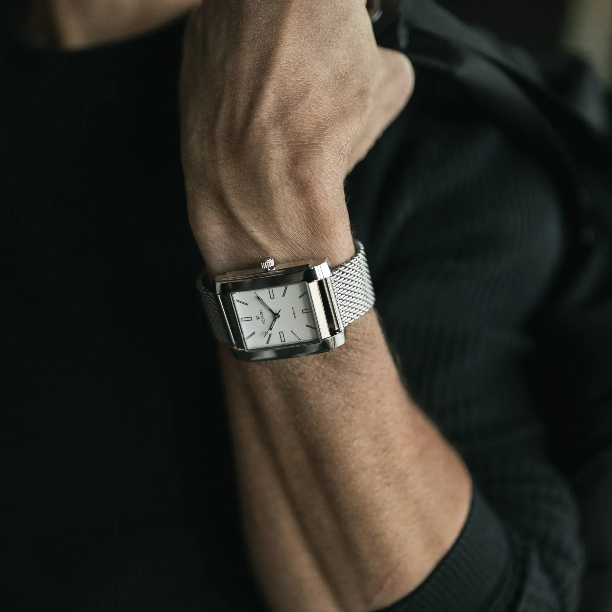 Legacy Prisma rectangular men's watch with a polished stainless steel case, white minimalist dial, and stainless steel mesh strap, worn on the wrist with a dark jumper.