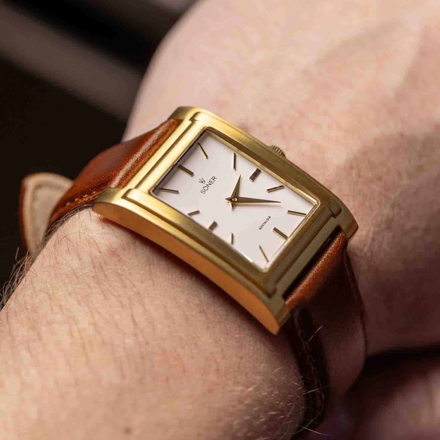 A close-up of a person’s wrist wearing the NOSTALGIA NICE 11-Year Battery watch featuring a gold rectangular case, brown leather strap, and white dial with minimalistic hour markers and hands.