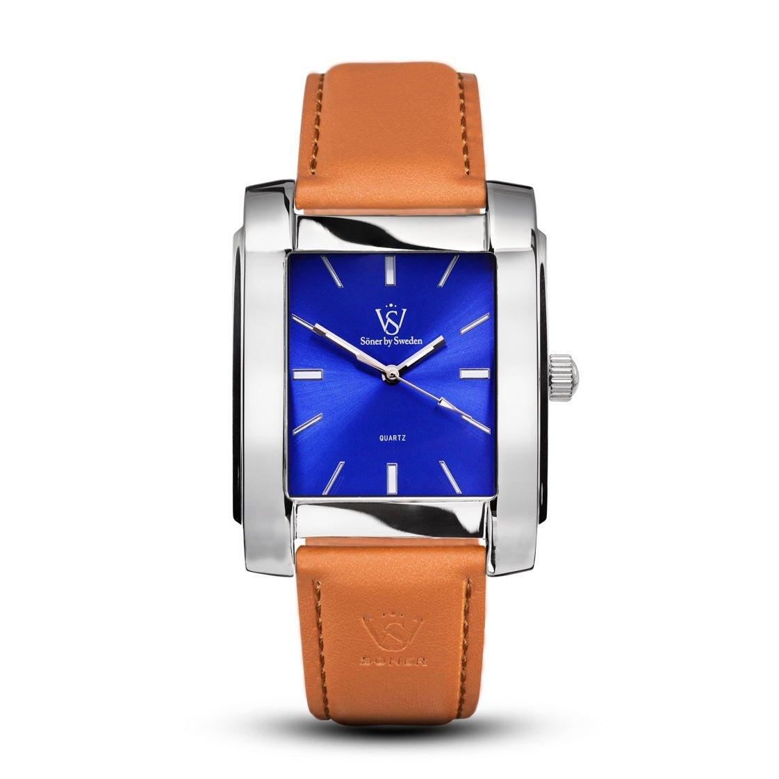 The Legacy Glocke (3-year Battery) from Söner showcases a blue dial adorned with silver hour markers and encased in a sophisticated silver frame. Its classic design is enhanced by a brown leather strap, with the logo prominently displayed at the top center of the dial, offering a perfect blend of timeless elegance and contemporary style.