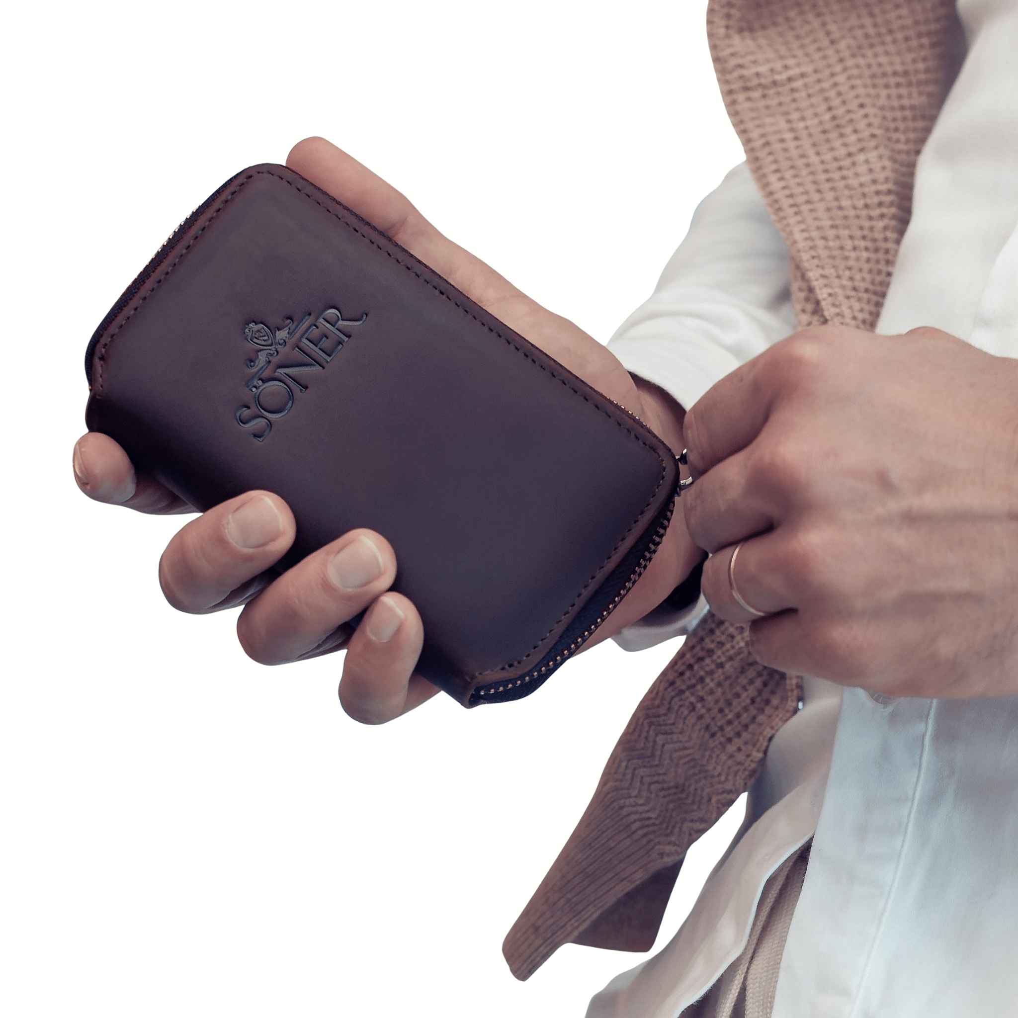 A person in a light shirt and beige textured jacket holds the Nostalgia Paris - Bundle wallet, a brown leather zippered accessory embossed with SONER. Save $50.